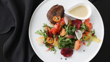 A plate with a salad, a meat patty, and a small bowl of sauce.