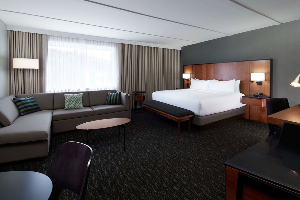 A hotel room with a bed, a sofa, a desk, a chair, and a small table.