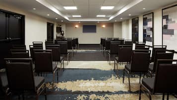 Un salón de conferencias con filas de sillas, una pantalla para proyector y piso alfombrado.