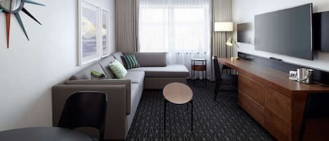A modern hotel room with a sofa, a small round table, a TV, and a cabinet.