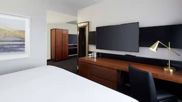 A hotel room with a large bed, a wooden desk, a flat-screen TV, a desk lamp, and a wardrobe.
