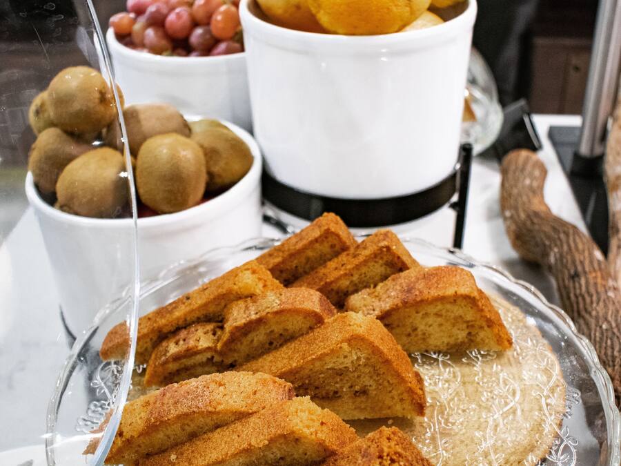 Una bandeja de vidrio con rebanadas de pastel, un tazón de kiwis, un tazón de uvas y un tazón de naranjas.