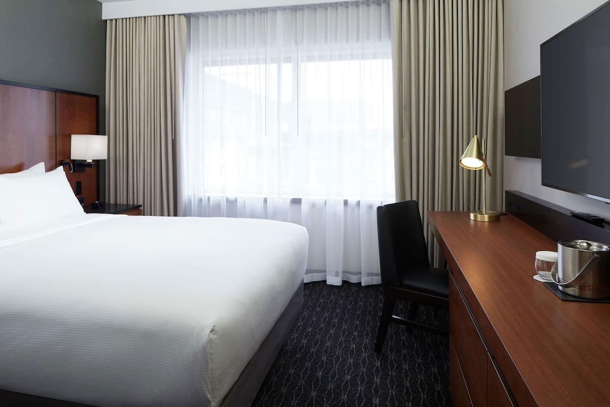 A hotel room with a large bed, a desk with a television, a chair, and a lamp.