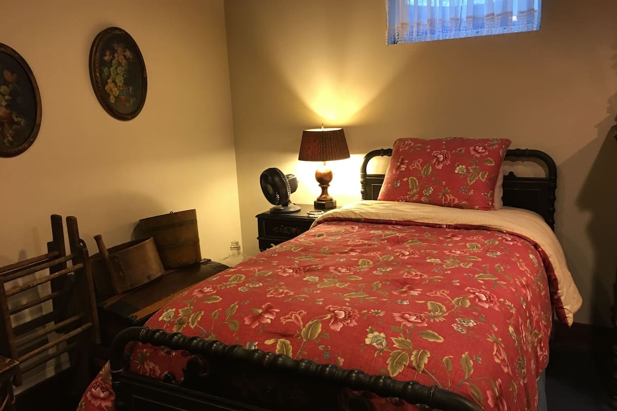 Une chambre à coucher comprenant un lit, une table de chevet, une lampe, une fenêtre et un mur orné de deux tableaux encadrés.