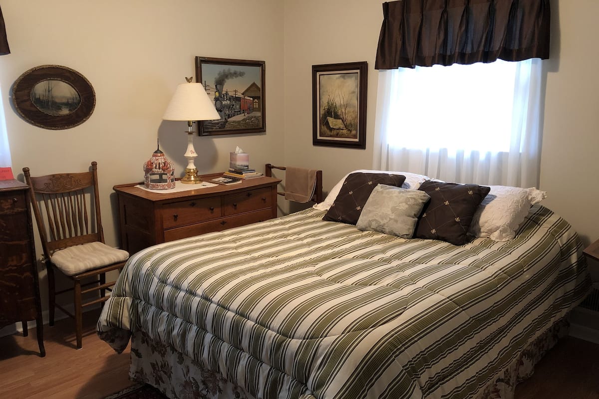 Une chambre à coucher comprenant un lit, une chaise, une commode et deux tableaux encadrés accrochés au mur.