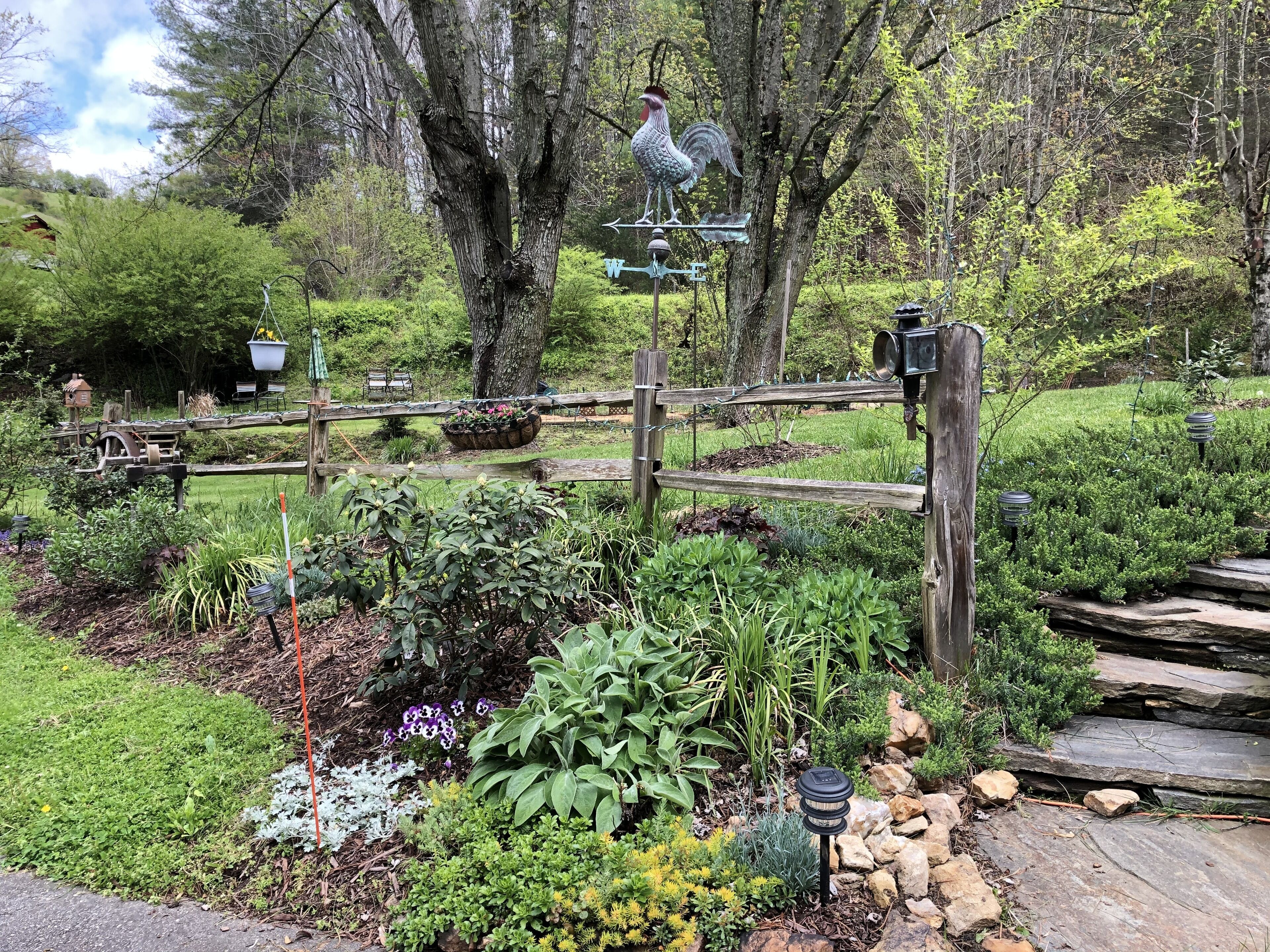 Un jardín con cerca de madera, veleta y estatua de gallo.