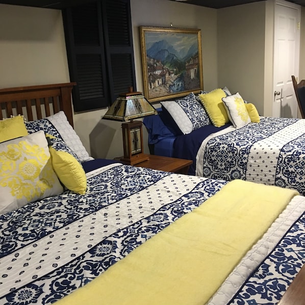 A hotel room with two beds, each with a blue and white patterned bedspread and yellow pillows. There is a wooden nightstand with a lamp between the beds, and a painting on the wall above the bed. - The Ashe Farm Bed & Breakfast (Marshall)