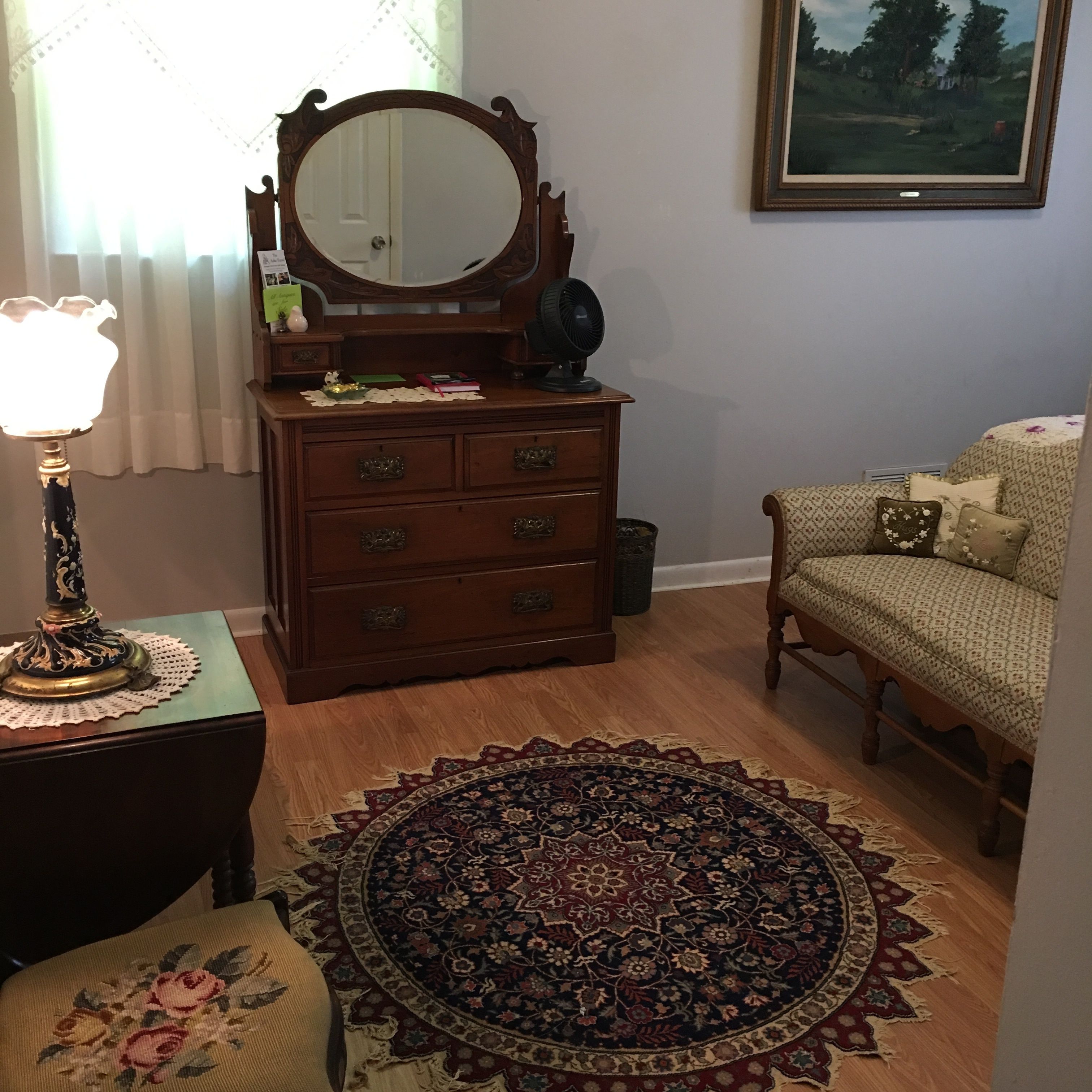 Una habitación con un aparador de madera, un espejo redondo, una lámpara, un tapete estampado y un sofá.