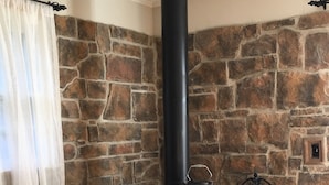 A stone fireplace with a black chimney, logs, and a cozy seating area.