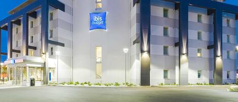 Un hotel moderno con un llamativo letrero de 'ibis budget', varios pisos y una entrada bien iluminada.