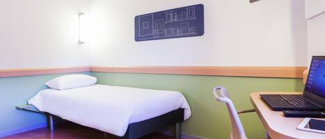 Una habitación de hotel con cama, escritorio con computadora portátil y televisor montado en la pared.