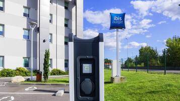 A parking area with a charging station, a building with multiple windows, and a sign that reads 'ibis budget.'