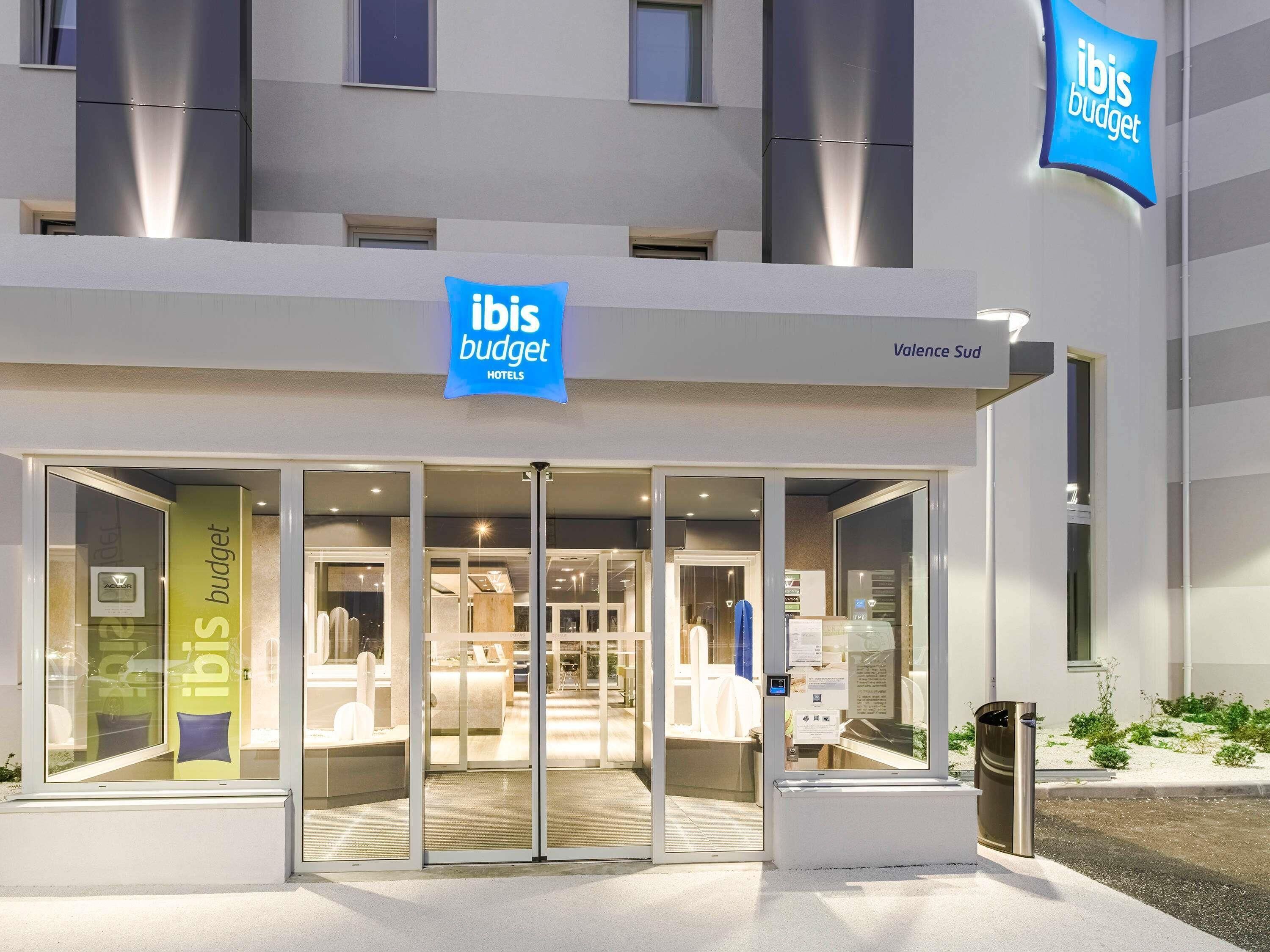 A modern hotel entrance with glass doors, a visible reception desk, and signage for 'ibis budget hotels.'