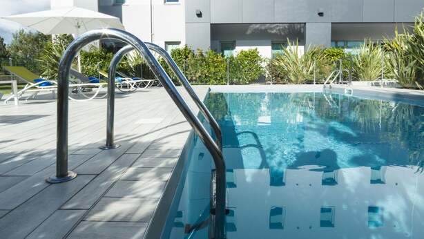 Un área de piscina moderna con agua azul cristalina, escalera metálica y sillas de descanso.