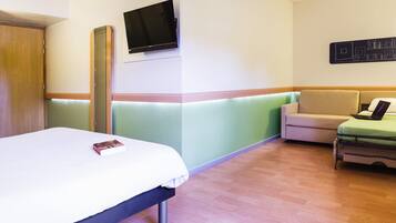 Une chambre d’hôtel avec un lit, un canapé, un téléviseur fixé au mur et une petite table avec un ordinateur portable.
