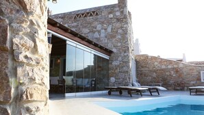 Ένα κτίριο από πέτρα με γυάλινη πόρτα, εξωτερικό χώρο για καθιστικό και μια πισίνα.