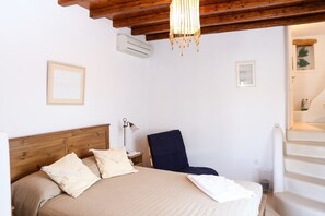 Une chambre à coucher avec une tête de lit en bois, un lit avec une literie beige, une chaise bleu foncé, une lampe sur pied et un escalier menant à un niveau supérieur.
