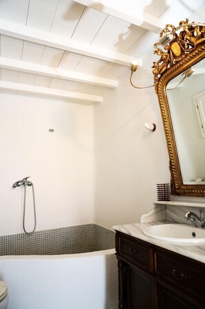 Une salle de bain avec une baignoire, un grand miroir doté d’un cadre orné et un lavabo blanc.