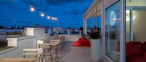 An outdoor seating area with tables and chairs, a red bean bag chair, and string lights against a twilight sky.