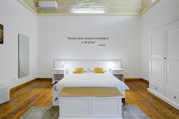 A modern hotel room with a large bed, bedside tables, a bench, and a quote on the wall.