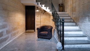 A staircase with a black metal railing, a brown leather armchair, and a vase with flowers on the landing. - Ada Suites (Lecce)