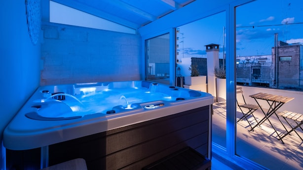 A modern hot tub with a glass enclosure, a foldable table, and chairs outside. - Ada Suites (Lecce)