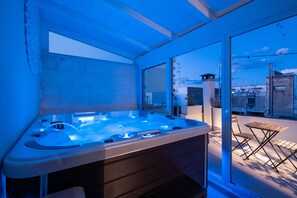 A modern hot tub with a glass enclosure, a foldable table, and chairs outside. - Ada Suites (Lecce)