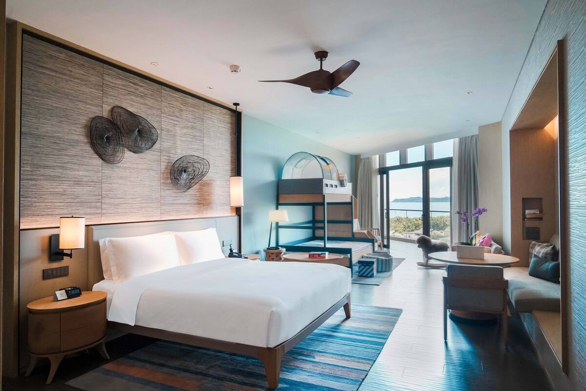 Ein modernes Hotelzimmer mit einem großen Bett, einem Schreibtisch, einem Stuhl und Blick ins Freie.