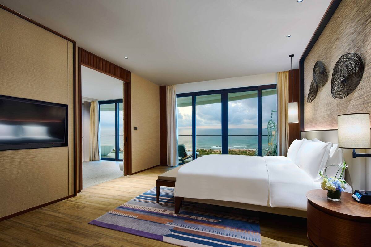 Ein modernes Hotelzimmer mit einem großen Bett, einem Flachbildfernseher, Meerblick und einem großen Fenster.