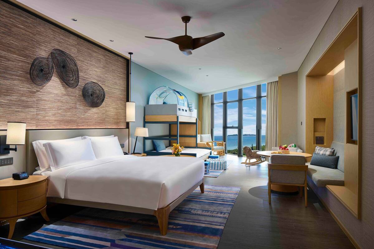 Ein modernes Hotelzimmer mit einem großen Bett, einem Deckenventilator, einer Sitzecke mit Blick und einem großen Fenster.