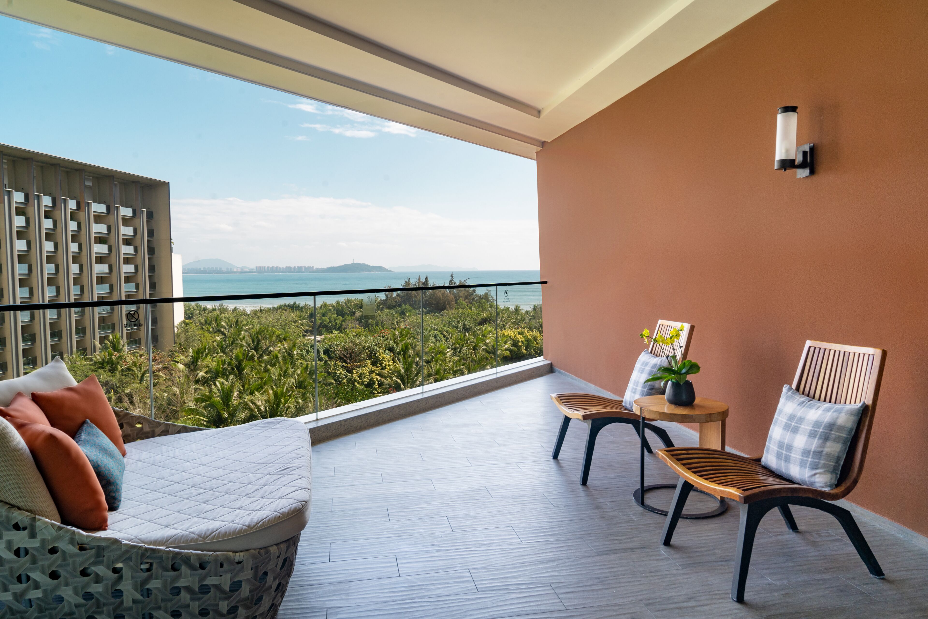 Ein Balkon mit Blick auf das Meer, ein Holzstuhl, eine gepolsterte Bank und ein kleiner Tisch mit einer Pflanze.