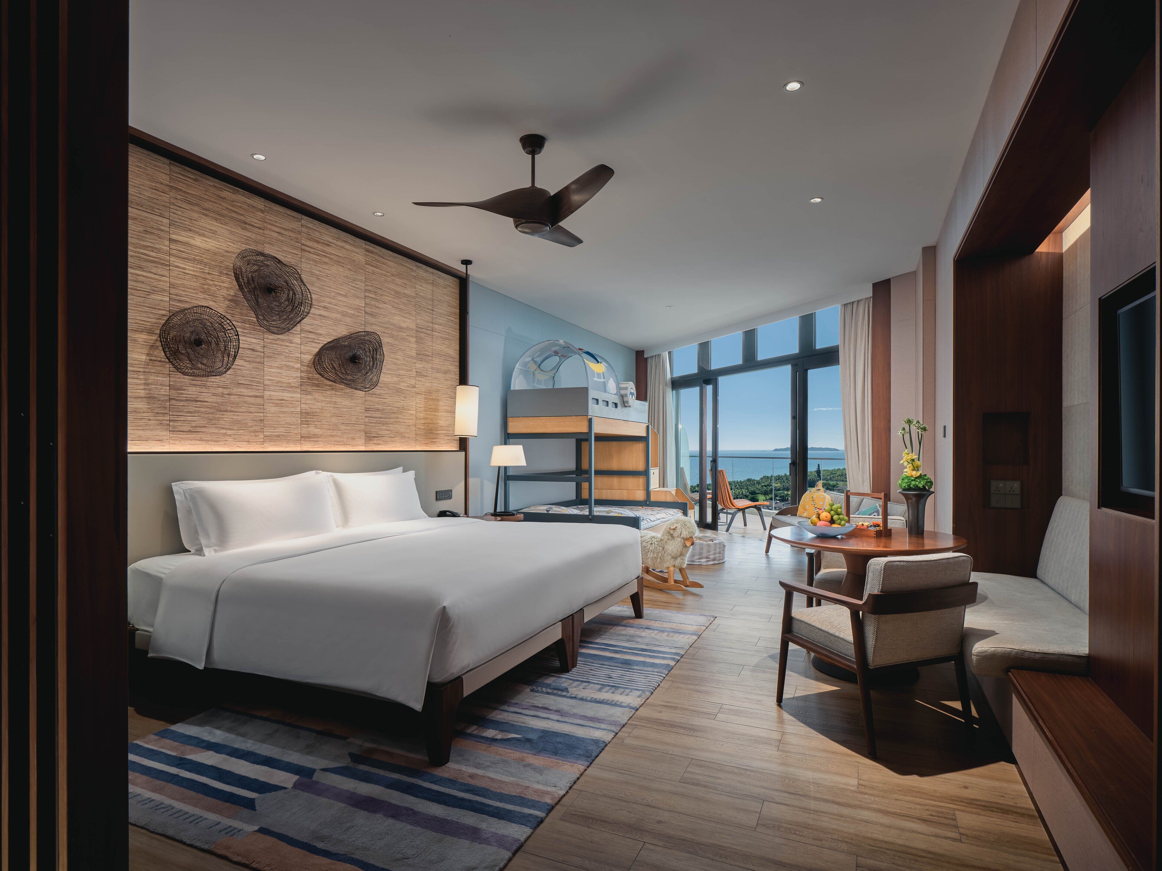 A modern hotel room with a large bed, a desk, and a balcony with a view.