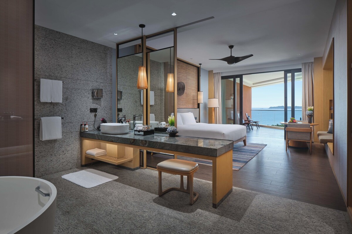 Habitación de hotel moderna con una cama grande, un escritorio separado, un baño con bañera y vista al mar.
