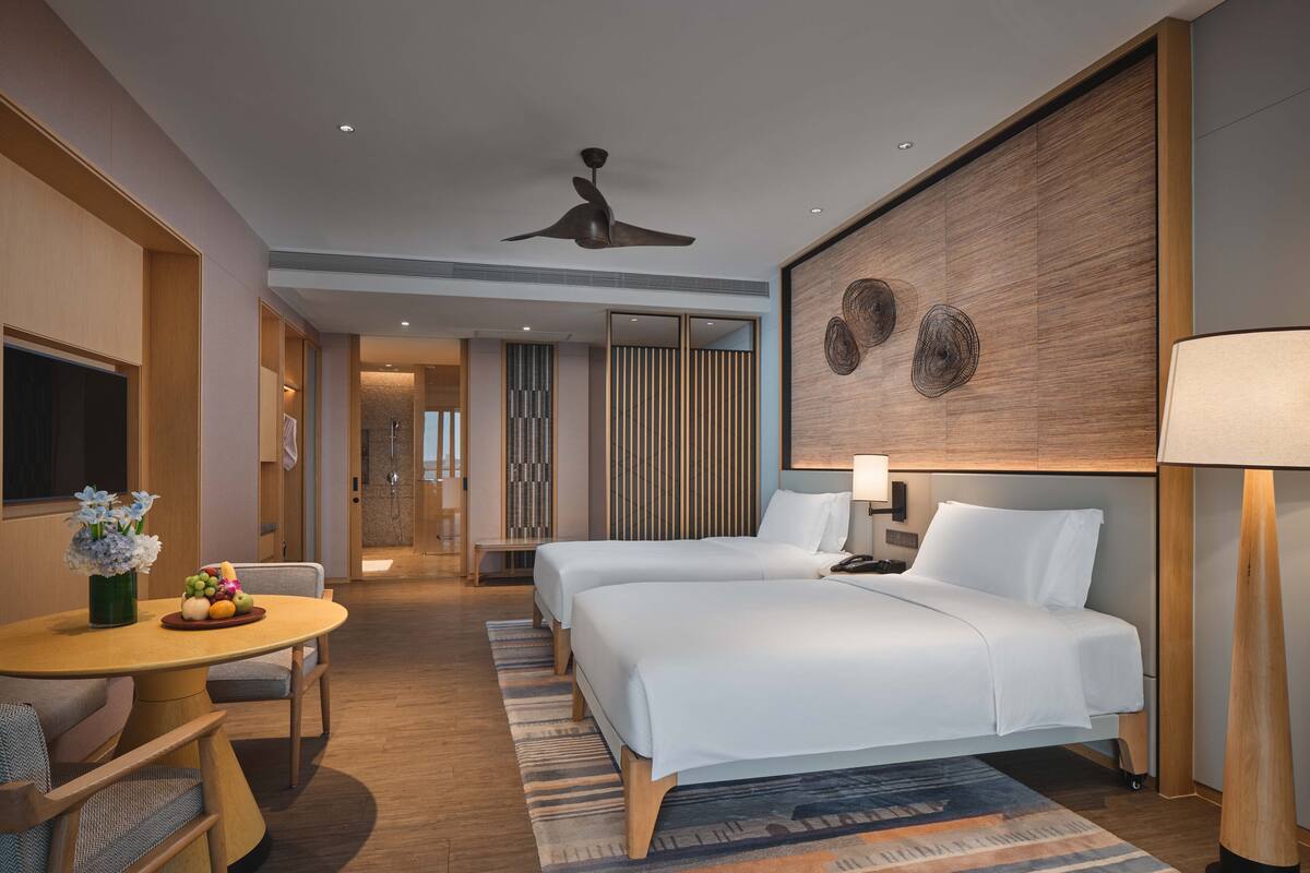 Ein Hotelzimmer mit zwei Betten, einem Essbereich inklusive Tisch und Stühlen, einer Duschkabine und einem großen Wandbild.