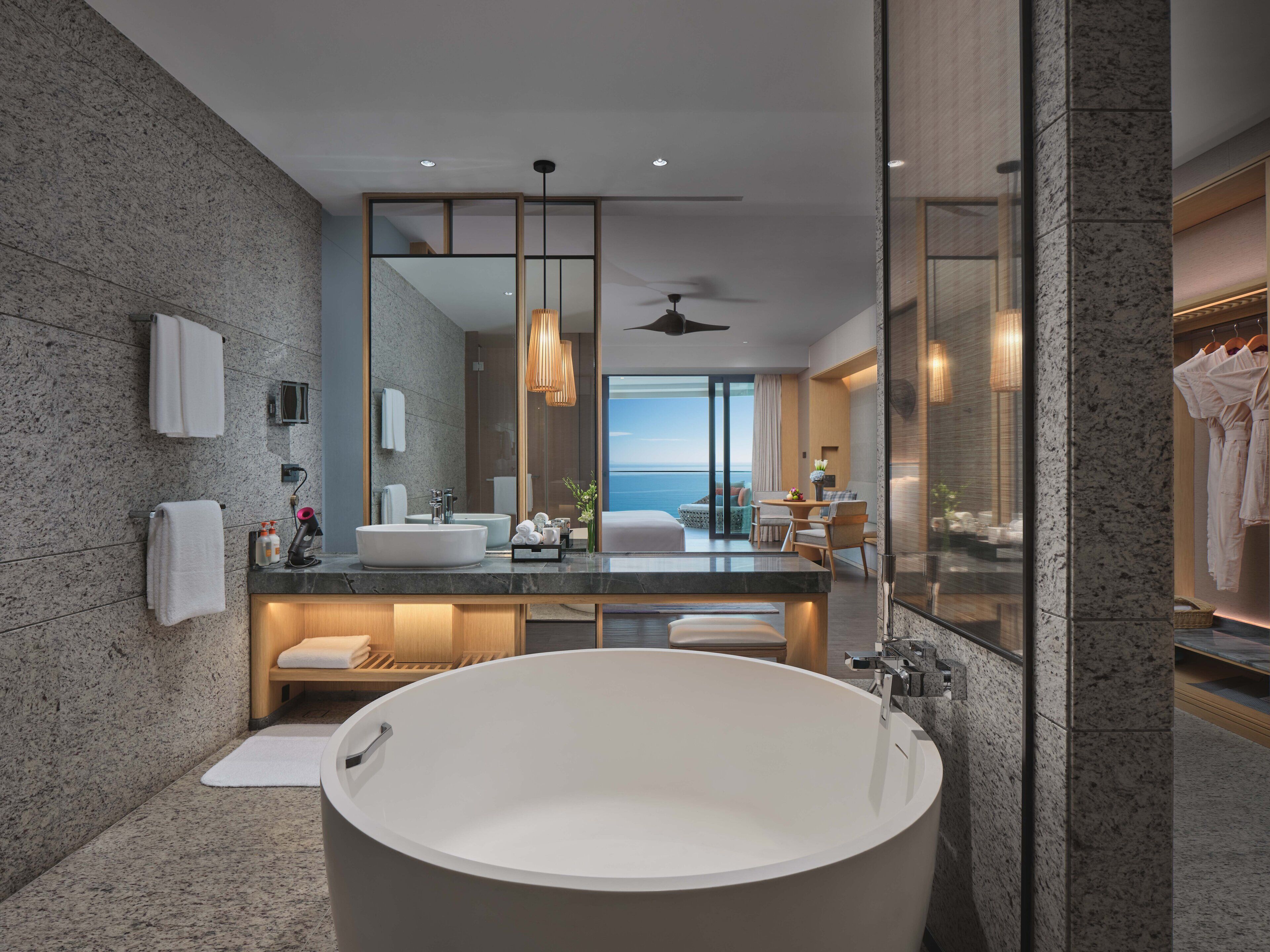 A modern bathroom with a large freestanding bathtub, a vanity with a mirror, and a view of the ocean.