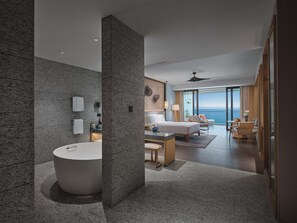 A modern hotel room with a large bathtub, a bed, a seating area with a view, and a balcony.