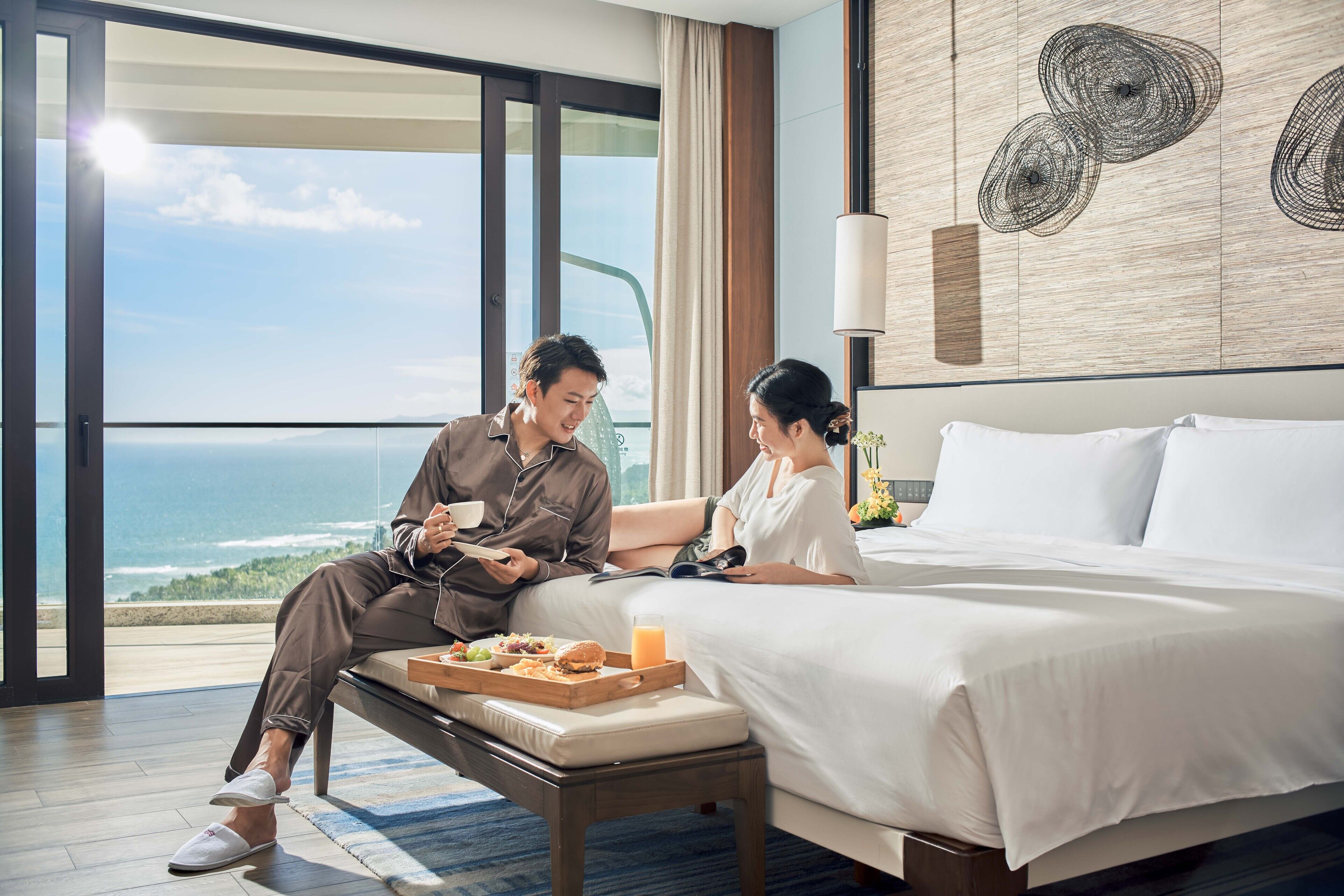 A hotel room with a large bed, a dining table with breakfast, and a view of the ocean.