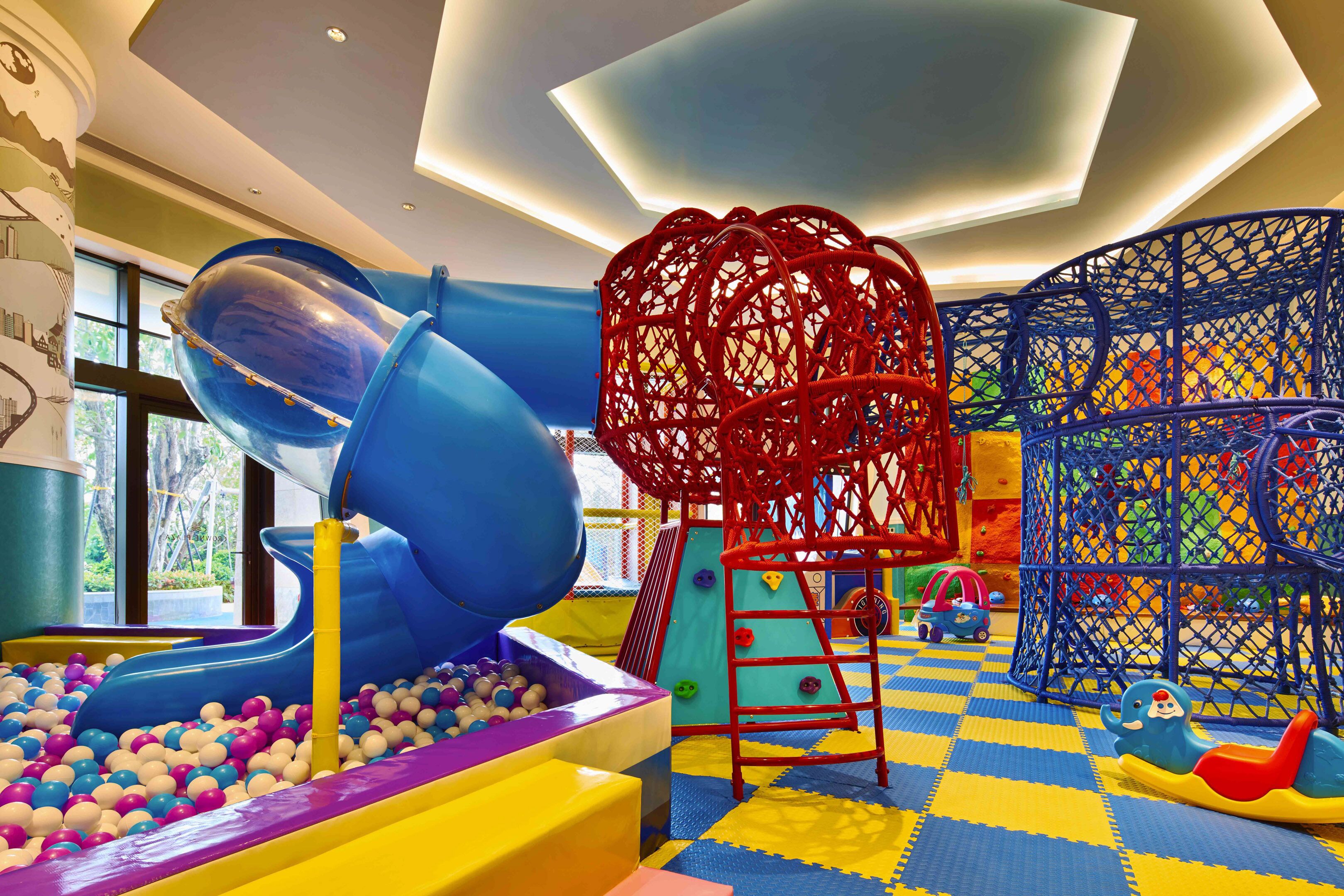 A children's play area with a blue slide, climbing net, and ball pit.