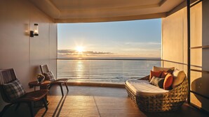 Un balcón con vistas al mar al atardecer, suelo de madera y mobiliario para sentarse.