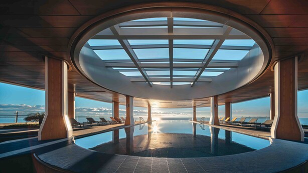 A circular infinity pool with a glass ceiling, surrounded by lounge chairs, and overlooking a scenic ocean view.