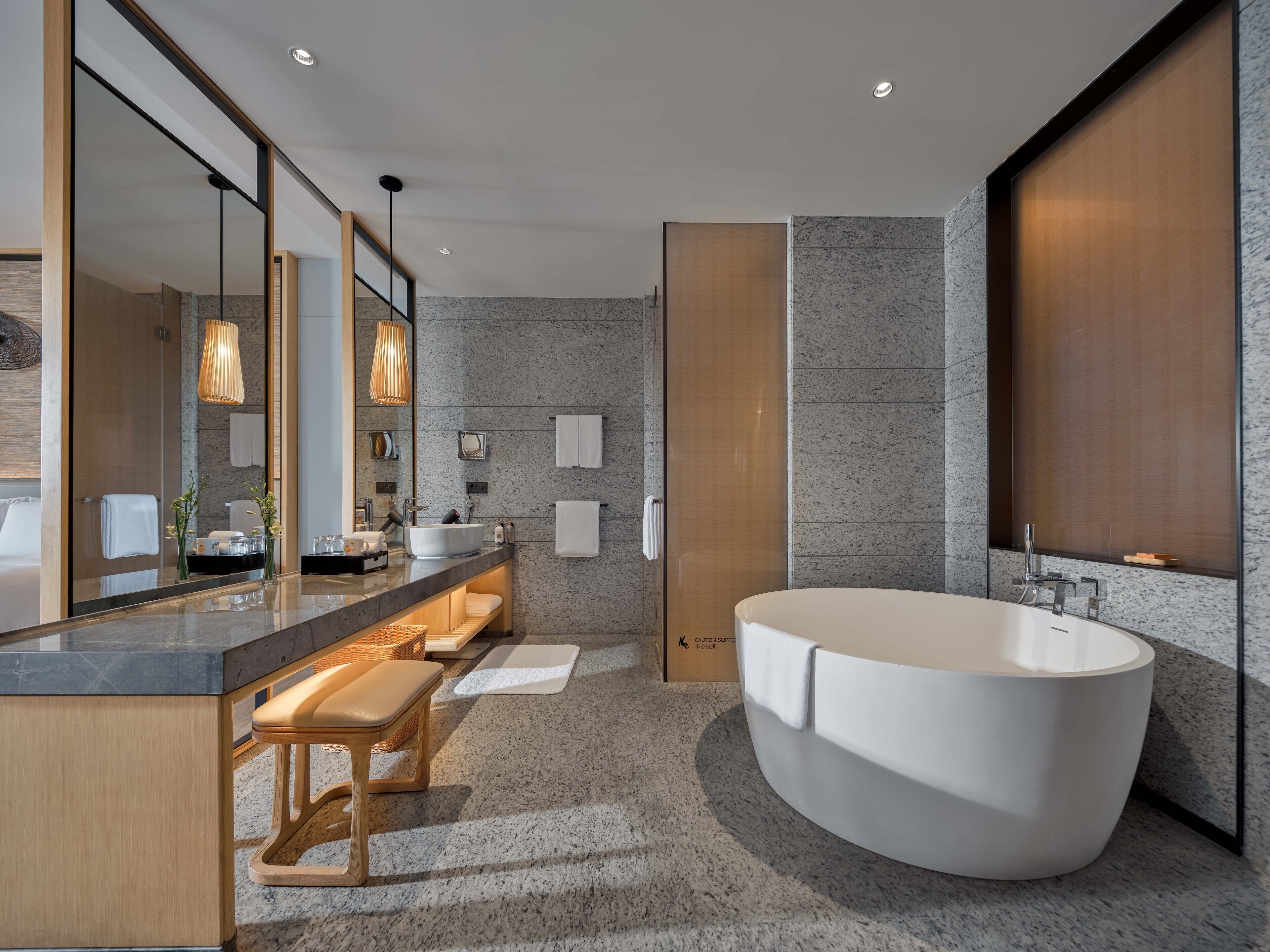 A modern bathroom with a freestanding bathtub, a large mirror, and a vanity with a bench.