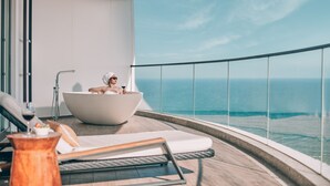 A balcony with a large bathtub, a lounge chair, and a view of the ocean.
