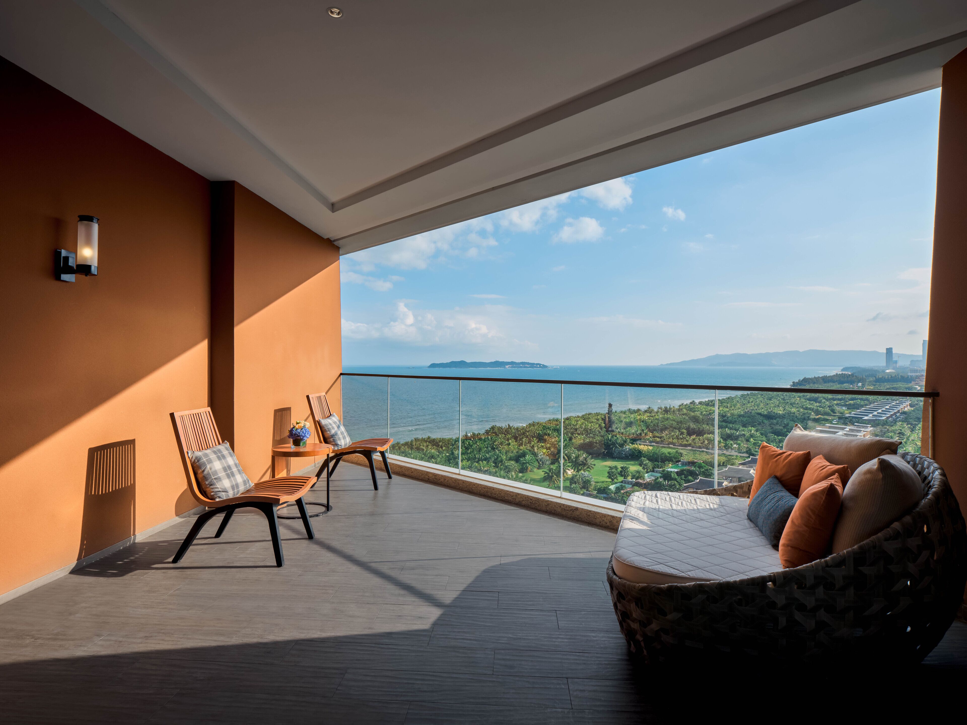 Uma varanda com vista para o mar e vegetação, mobiliada com sofá e cadeiras.