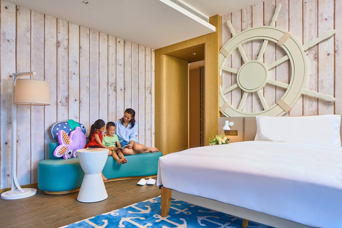 Ein Hotelzimmer mit einem Bett, einer großen Schiffsschwengel an der Wand, einer Wandverkleidung aus Holz, einem türkisfarbenen Sofa und einem kleinen weißen Tisch.