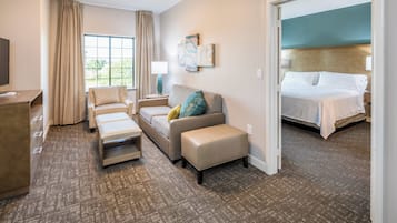 Una habitación de hotel con sofá, una mesita, un banco, cama y televisor.