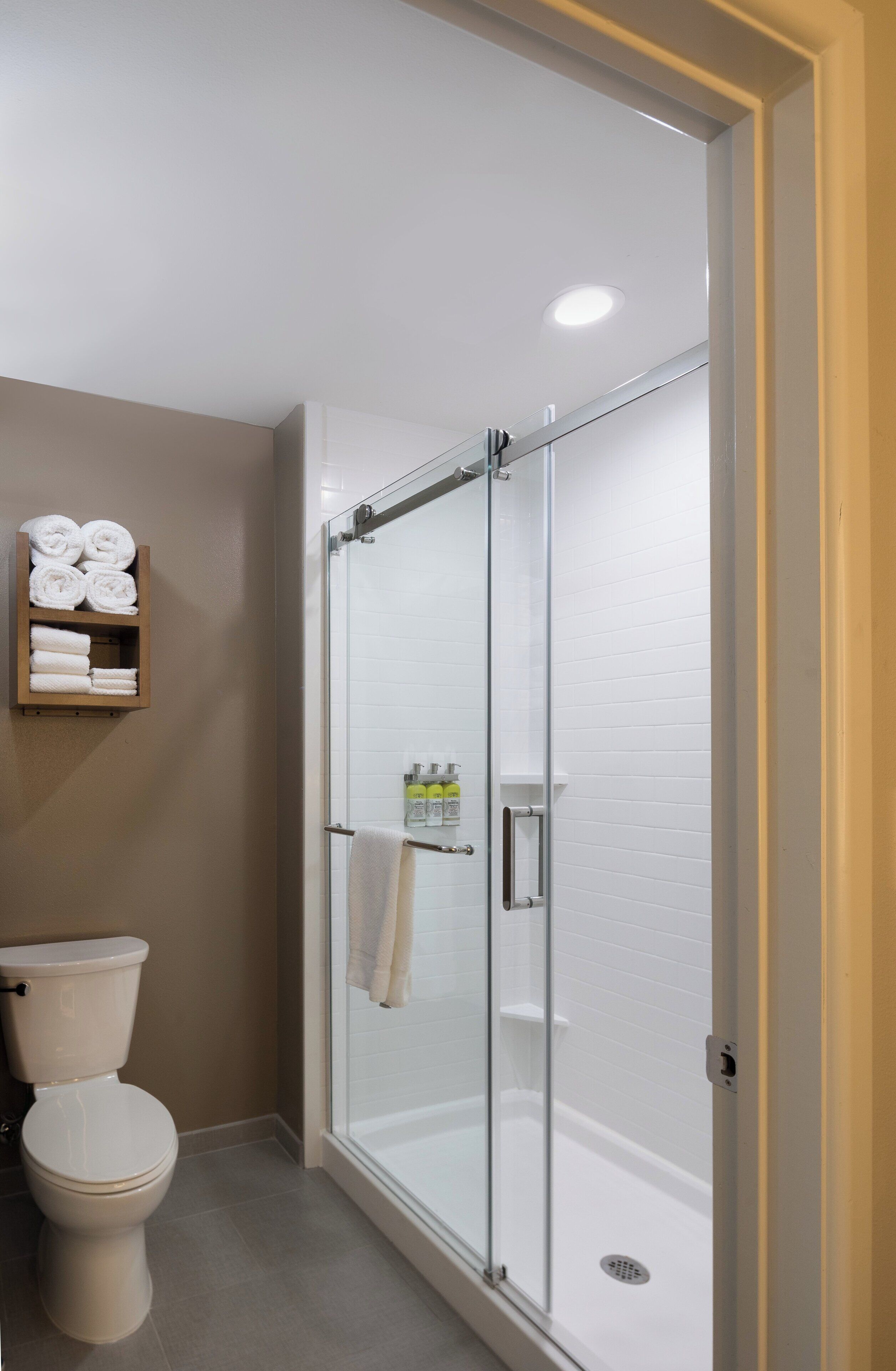 A bathroom with a glass-enclosed shower, a toilet, and a shelf with towels.