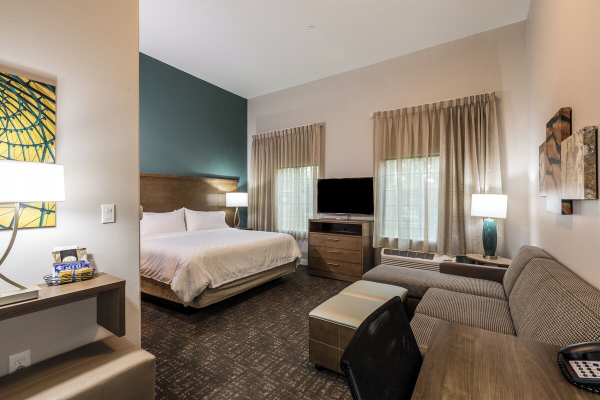 A hotel room with a bed, a TV, a sofa, a desk, and a lamp.