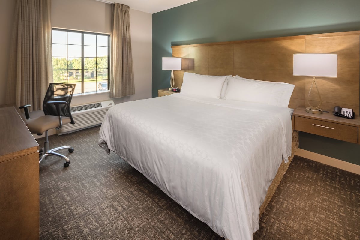 A hotel room with a large bed, a desk, a chair, a window with curtains, and two bedside lamps.