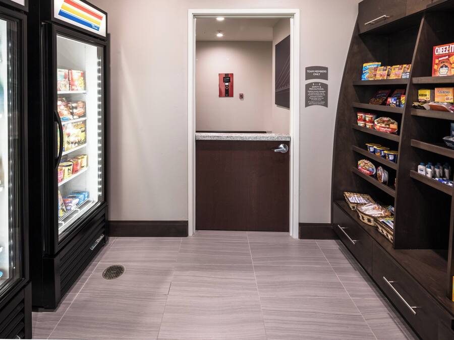 A hotel corridor with a refrigerator stocked with beverages, a pantry with snacks, and a door leading to another room.