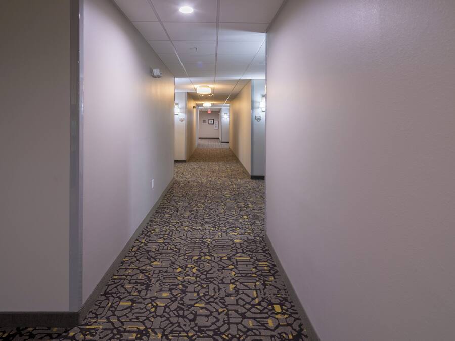 Un pasillo de hotel con alfombra estampada, paredes blancas e iluminación empotrada en el techo.